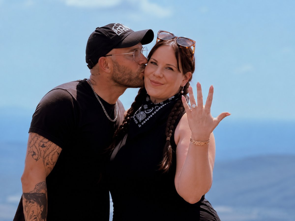 Whitney Thore shows off her engagement ring as fiance Jake Beaudoin kisses her cheek in the Blue Ridge Mountains