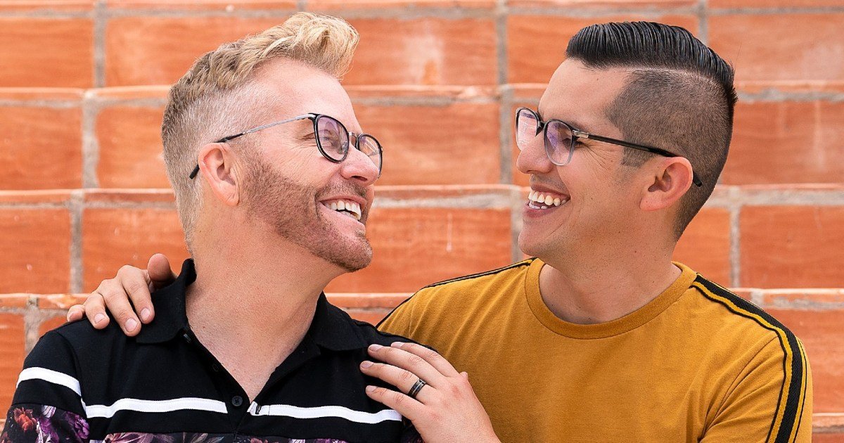 Kenny Niedermeier and Armando Rubio laughing together in front of a red brick wall