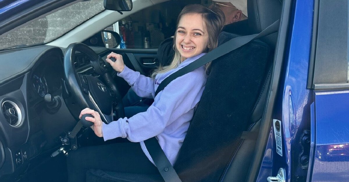 Shauna Rae smiling in the driver's seat of a car with hand controls