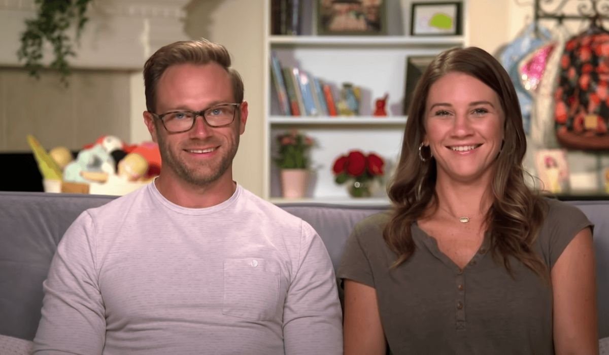 Adam and Danielle Busby smiling together on the sofa